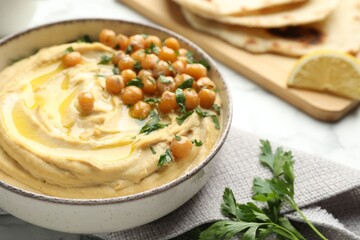 Delicious hummus with olive oil, chickpeas and parsley in bowl on table, closeup