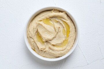 Delicious hummus with olive oil in bowl on white textured table, top view