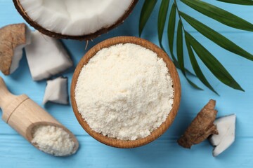 Fresh coconut flour in bowl, scoop, nut and palm leaf on light blue wooden table, flat lay