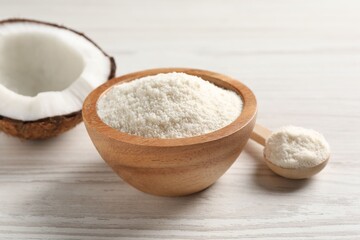 Fresh coconut flour in bowl, spoon and nut on white wooden table