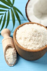 Fresh coconut flour in bowl, scoop, nut and palm leaf on light blue wooden table