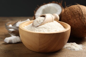 Coconut flour in bowl, scoop and fresh fruits on wooden table, closeup