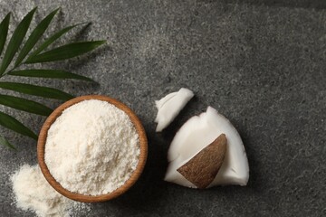 Organic coconut flour in bowl, fruit pieces and leaf on grey table, flat lay. Space for text
