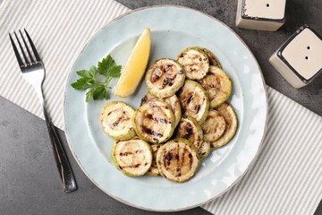 Tasty grilled zucchini slices served on grey textured table, flat lay