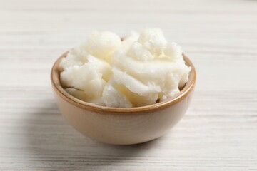 Shea butter in bowl on white wooden table, closeup