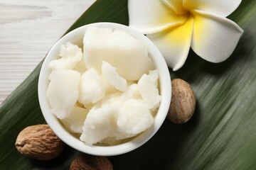 Shea butter in bowl, flower and nuts on white wooden table, flat lay