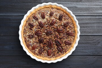 Delicious pecan pie in baking dish on dark wooden table, top view