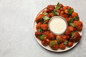 Baked cauliflower buffalo wings with parsley and sauce on light grey table, top view. Space for text