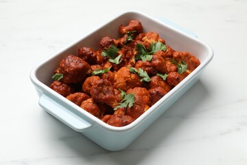 Baked cauliflower buffalo wings with parsley in baking dish on white marble table