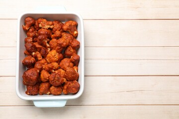 Baked cauliflower buffalo wings in baking dish on wooden table, top view. Space for text