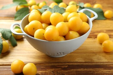 Tasty ripe plums and leaves in colander on wooden table, closeup