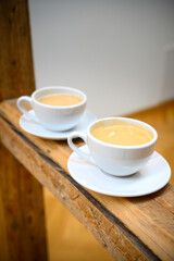 Two cups of hot coffee with milk stand one behind the other on old rustic wooden beams in a house with exposed timber framing. Charming office on vertical picture