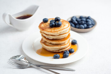 Breakfast buttermilk pancakes with blueberries and maple syrup stacked on white plate, closeup view
