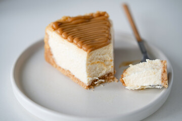 Cheesecake with caramel sauce topping, missing a bite. White plate. Closeup view