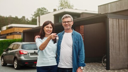 Happy Caucasian couple cuddling each other while standing before their new estate. Beautiful wife...