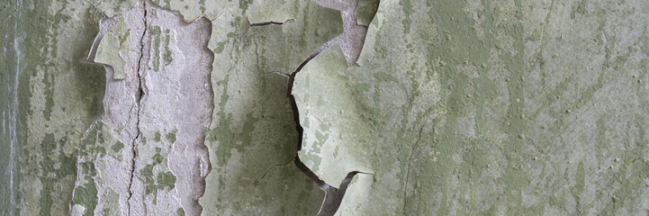 Peeling paint on the wall. Panorama of a concrete wall with old cracked flaking paint. Weathered rough painted surface with patterns of cracks and peeling. Grunge texture for wide panoramic background