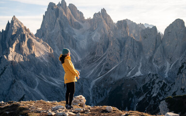 A woman hikes in the mountains, her attire suitable for the crisp atmosphere, as she observes the...