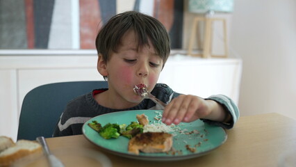 Young boy eating lunch at home, enthusiastically using a fork, capturing the playful and joyful...