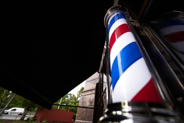 Classic barber pole stands outside a barbershop on a sunny day
