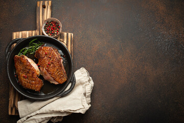Two roasted duck breast fillets with crispy skin, with pepper and rosemary, top view in black cast...