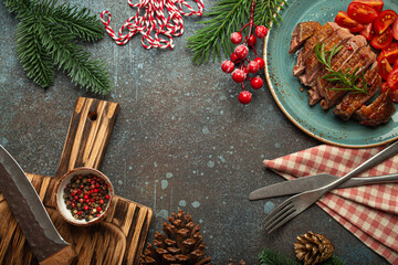 Festive Christmas dinner boarder background with space for text with roasted duck breast fillet with golden crispy skin and tomato salad, Xmas decorations with fir tree, cones, red berries..