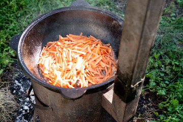 frying chopped carrots in a cast iron cauldron over a fire to prepare pilaf