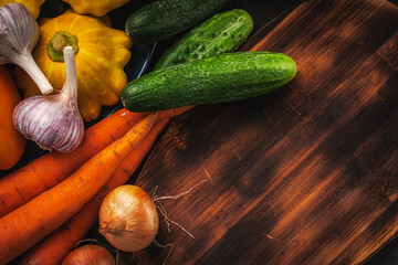 Assorted raw, organic vegetables with a wooden plank. Cucumbers, carrots, pumpkin, onions and garlic on the table. A place to copy the space.