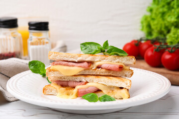 Pieces of toasted bread with melted cheese, ham and basil on white table