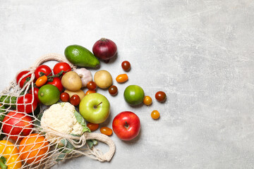 Vegan food delivery. Net bag with different fresh vegetables and fruits on grey textured table, flat lay. Space for text