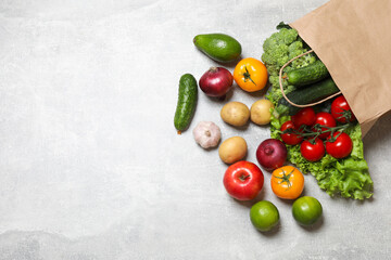 Vegan food delivery. Paper bag with different fresh vegetables and fruits on grey textured table, flat lay. Space for text