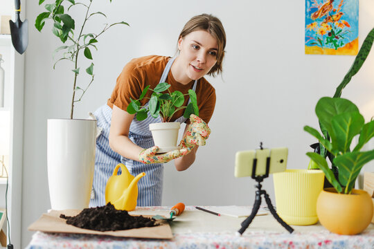 Gardener woman holding plant recording video blog using smartphone on tripod