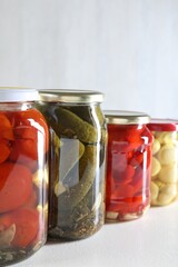 Tasty pickled vegetables and mushrooms in jars on white background, closeup