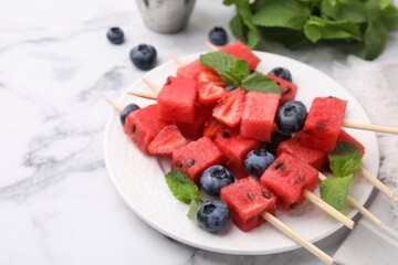 Skewers with tasty watermelon, strawberries, blueberries and mint on white marble table, closeup