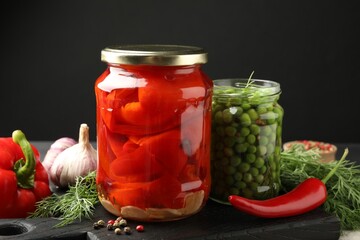 Different pickled products in jars and fresh ingredients on table, closeup