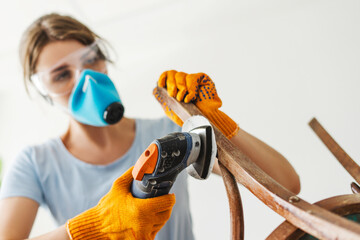 Woman restoring wooden chair using electric sander wearing safety equipment