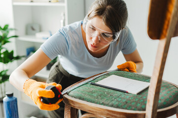Woman wearing safety glasses taking measurements of an old chair using a tape measure