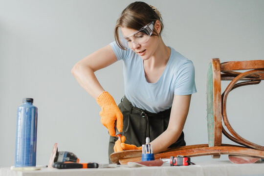 Woman restoring old furniture using screwdriver in workshop