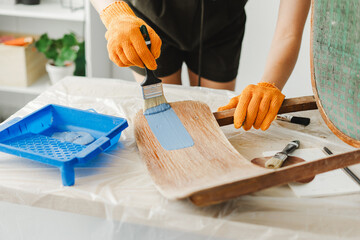 Woman restoring old furniture painting wooden surface with blue paint