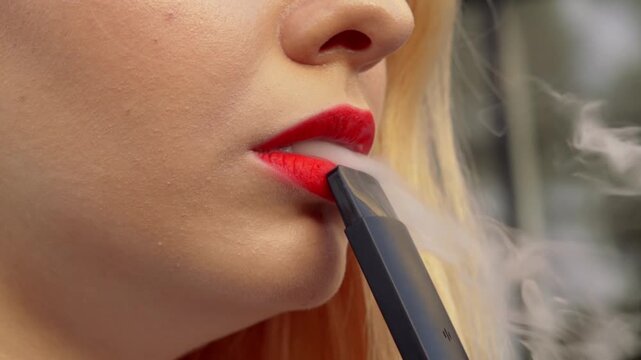 Young pretty woman standing outside street having break smoking trendy tobacco device electronic cigarette heater vape. Smoke and steam system with sticks inside. Harmful habit harm to health lungs