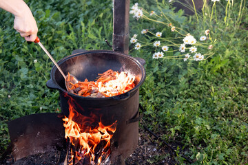 stir chopped carrots in a cast iron cauldron over a fire to prepare pilaf while frying outdoors