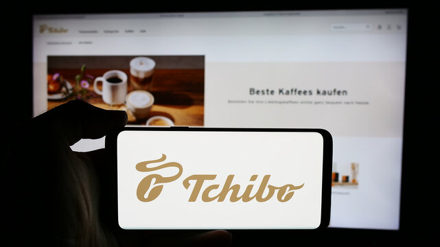 Stuttgart, Germany - 08-07-2024: Person holding cellphone with logo of German coffee retail company Tchibo GmbH in front of business webpage. Focus on phone display.