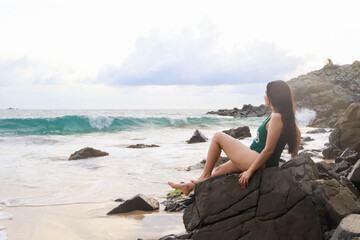 Woman on a rock watching at the landscape in the beach. Watching the waves and blue water.