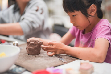 Young girl deeply engrossed in shaping clay during an art project. Her intense creativity are...