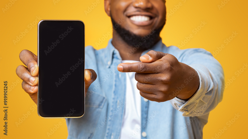Poster check this app. cheerful afro guy holding and pointing at smartphone with black screen, yellow backg