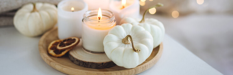 Autumn home decor with white pumpkins and burning aroma candles with sweet spicy pumpkin pie scent. Cozy fall composition, relaxation, aromatherapy. Apartment design, living room or bedroom banner