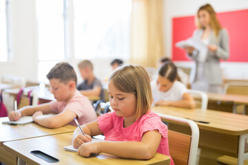 Portrait of cute intelligent schoolgirl who writing exercises at lesson in primary school © JackF