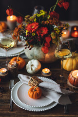 Beautiful elegant table setting for candlelight Thanksgiving Day dinner or Halloween party at home. Fancy dishware, porcelain plates. Floral centrepiece, pumpkins and burning candles as decor