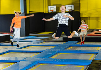 Smiling school-age girl in striped T-shirt and black shorts jumping and indulging on trampolines in entertainment center. Active leisure concept