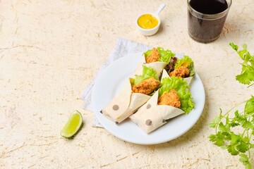 Mini tortilla wraps filled with fried chicken, cheese, salad and mustard sauce on a white plate on...