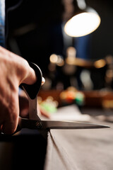 Skillful craftsman using scissors to cut refined fabric material in tailoring studio, making premium quality sartorial collection. Precise suitmaker handcrafting bespoke business suit piece, close up